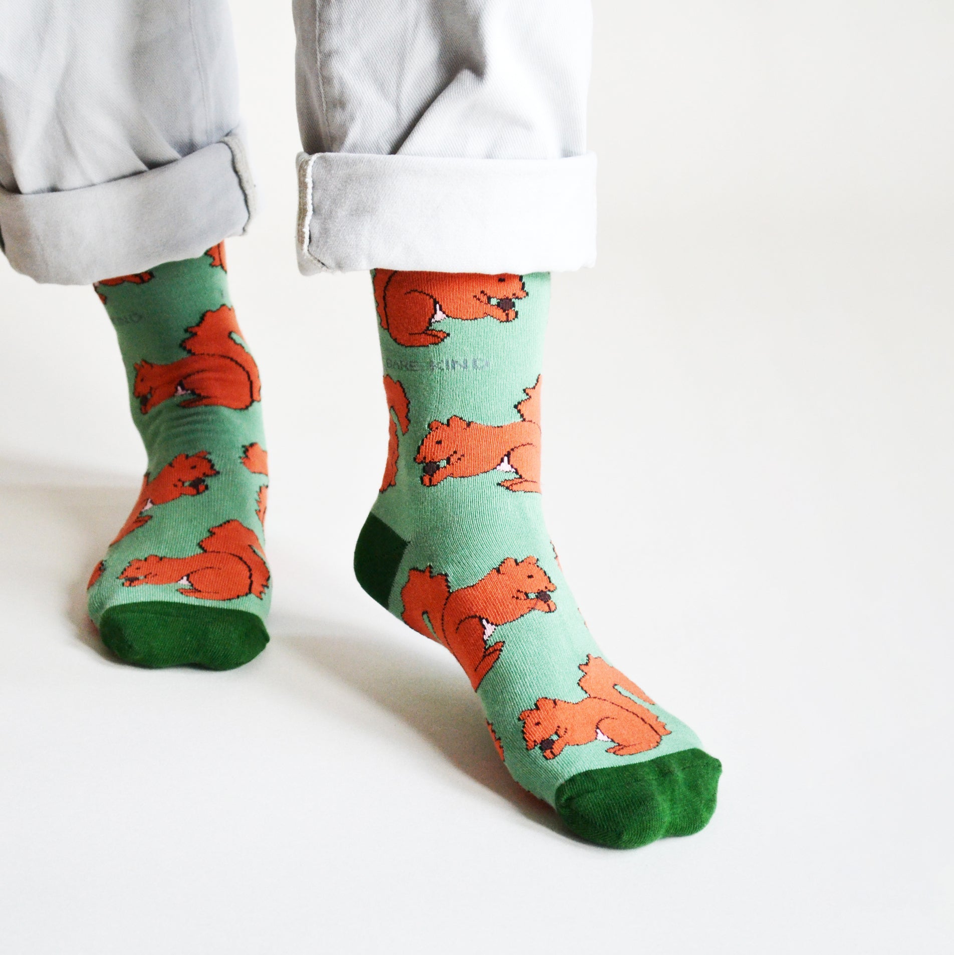 Green socks with red squirrel patterns worn by a person on a white background