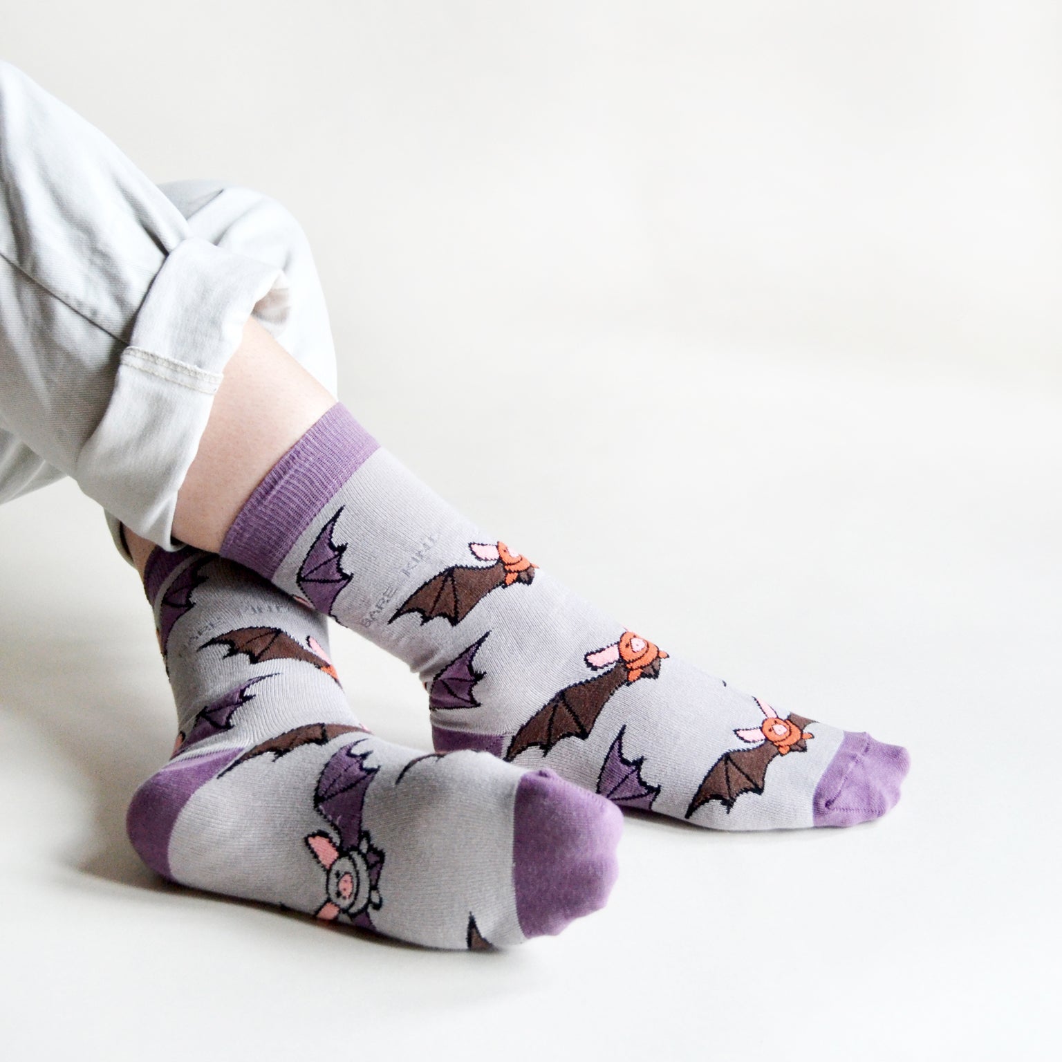 Person sitting wearing Purple Bare Kind socks with bat print.