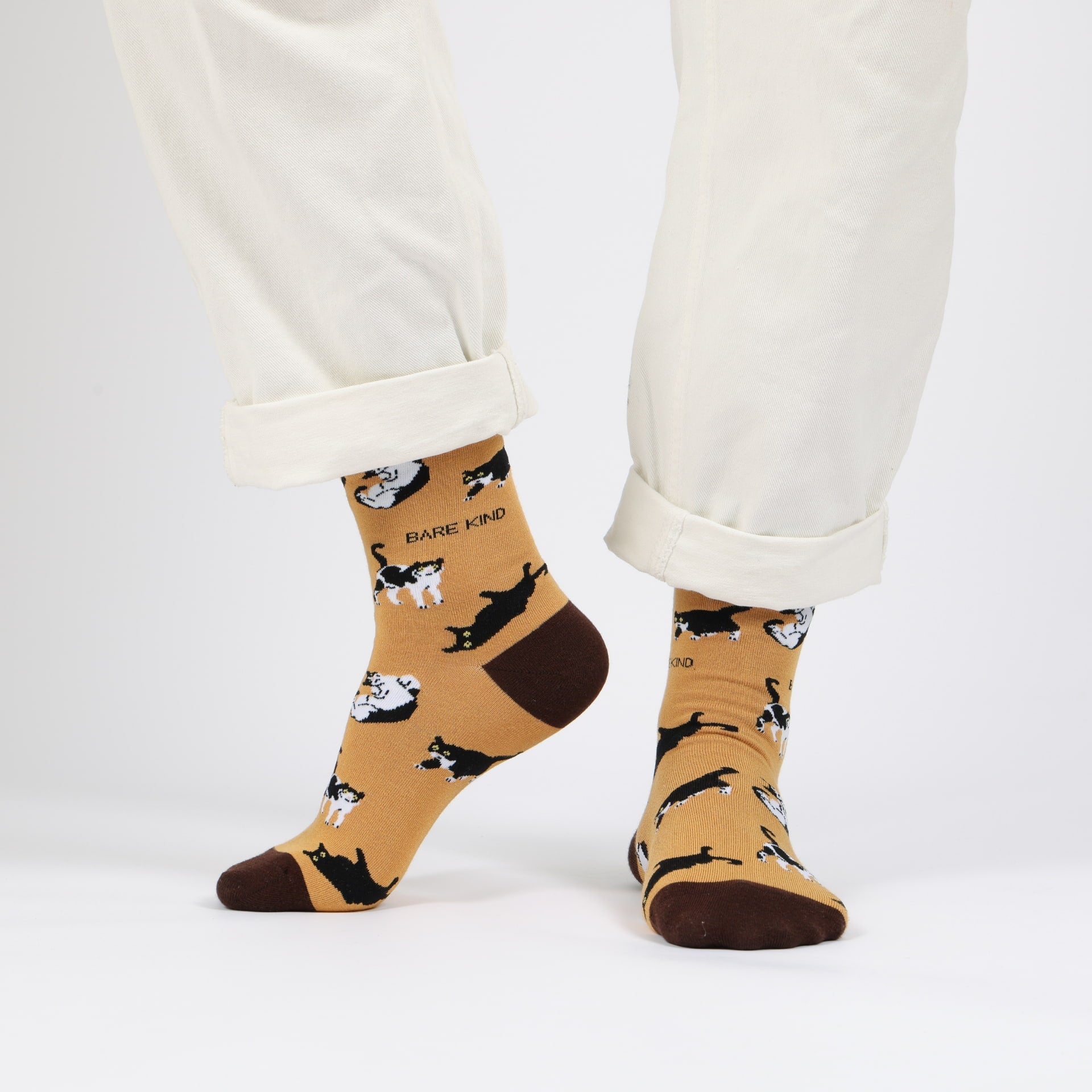 Beige socks with black cat pattern worn with white pants on a light gray background