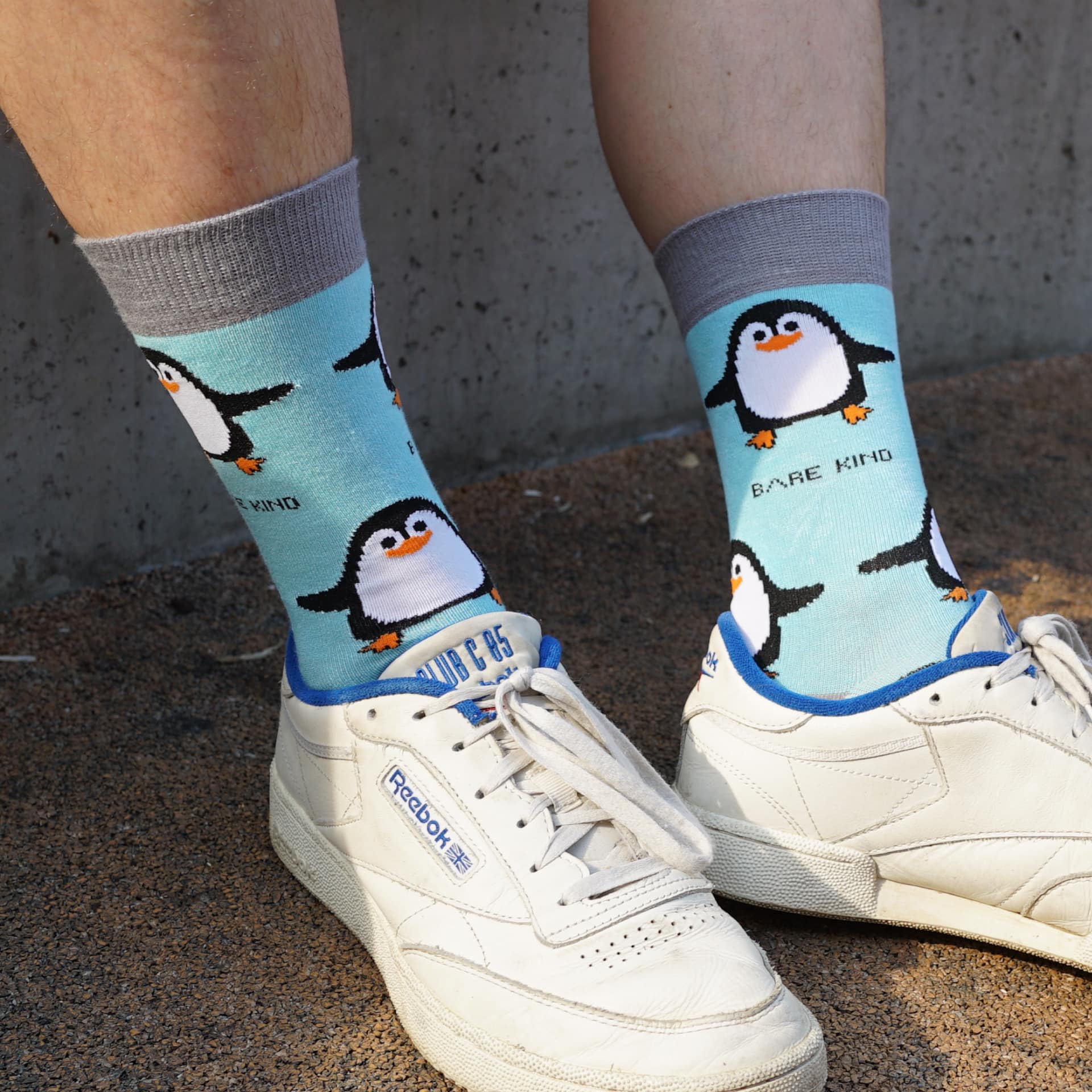 Person wearing socks with penguin design and white sneakers on a concrete floor.