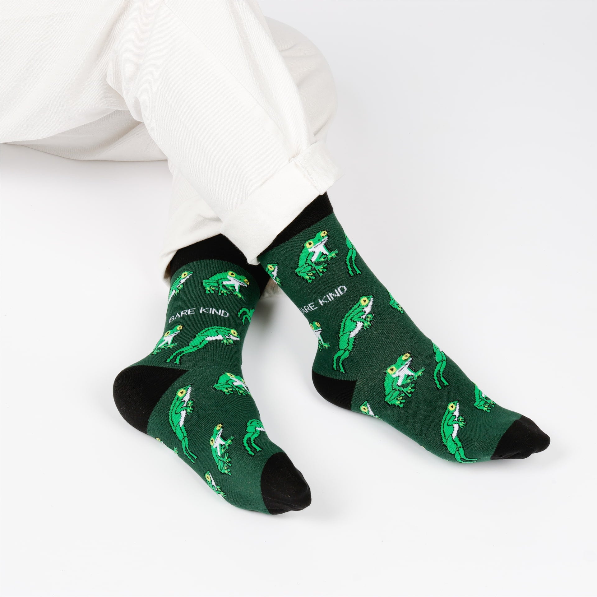 Green socks with frog pattern and 'Be Kind' text on a white background