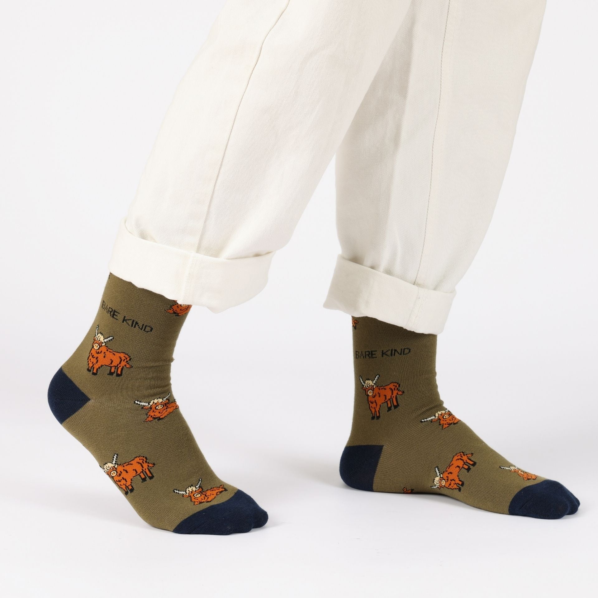 Green socks with fox design and 'Be Kind' text worn with white pants on a white background