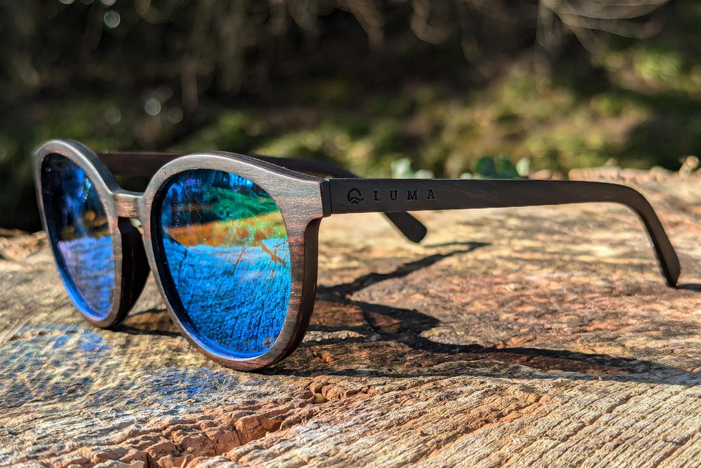 Wooden sunglasses with blue reflective lenses on a textured surface