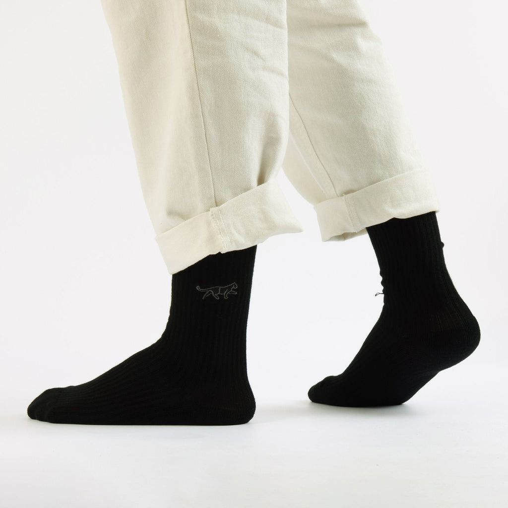 Person standing wearing Black Bare Kind socks with panther print.