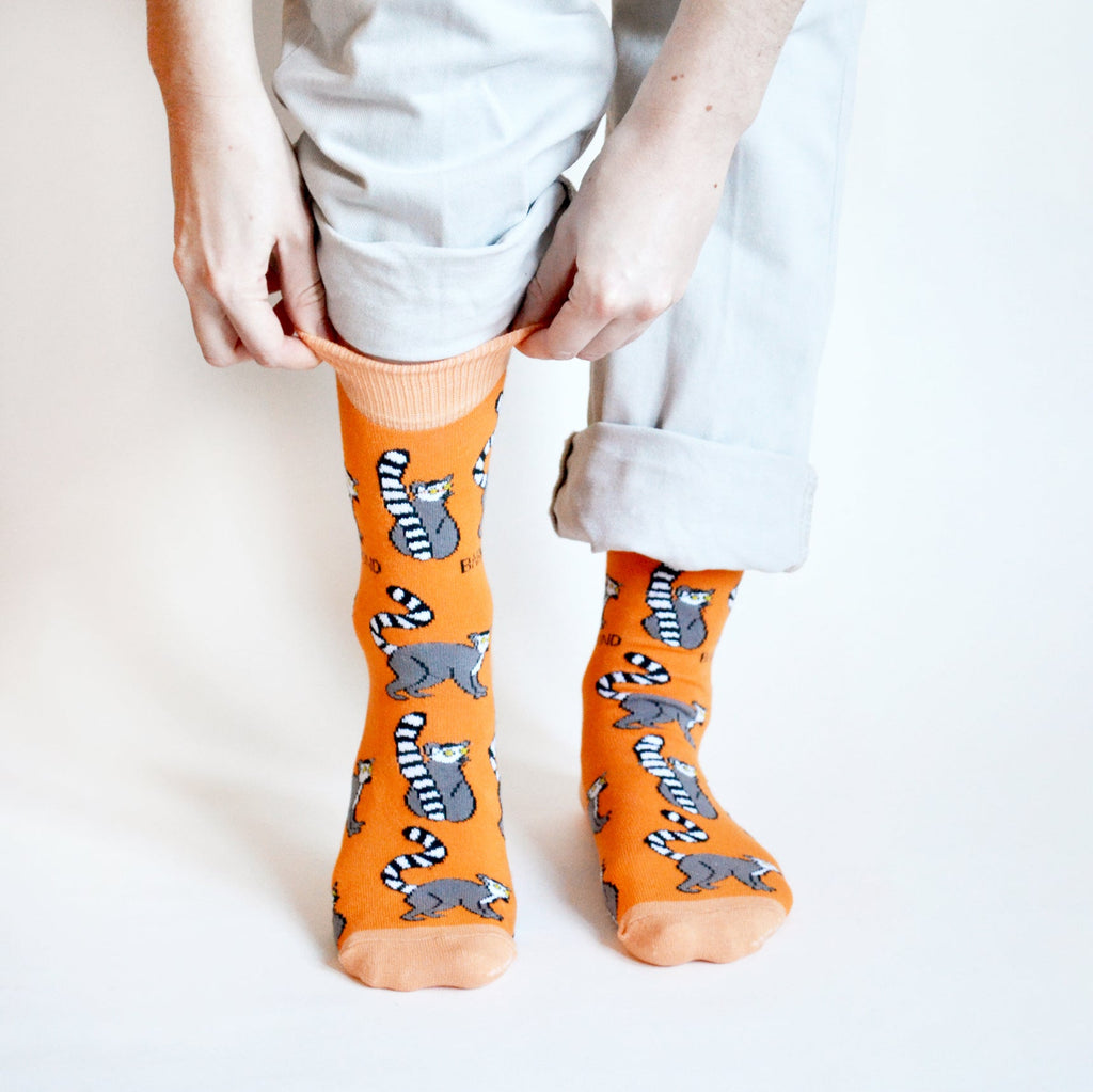 Person standing wearing Orange Bare Kind socks with lemur print.