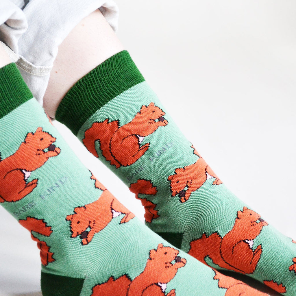 Green socks with red squirrel  pattern worn by a person on a white background