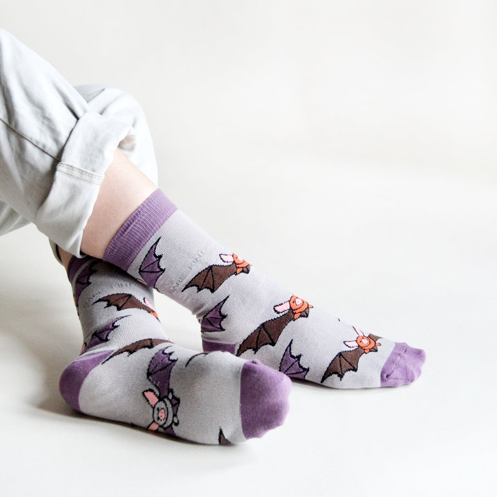 Person sitting wearing Purple Bare Kind socks with bat print.