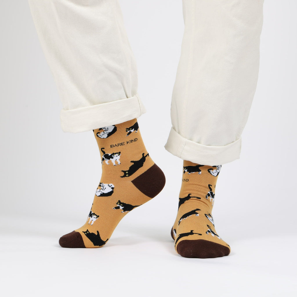 Beige socks with black cat pattern worn with white pants on a light gray background