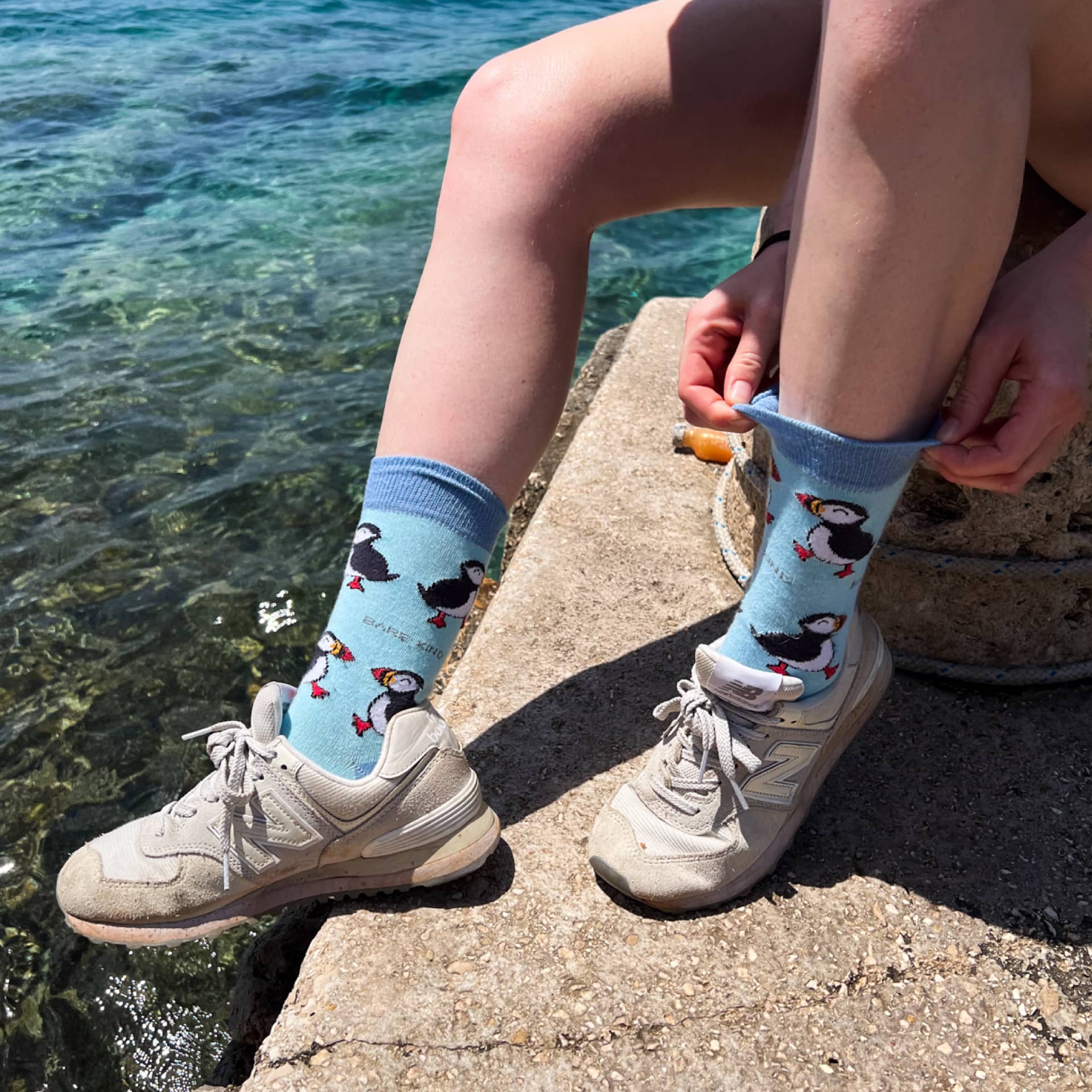 Person wearing blue socks with puffin design by a body of water.